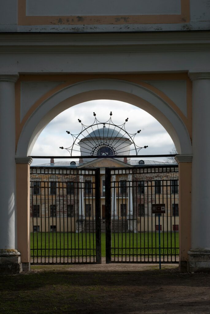 Ornamental iron gate framed by archway, revealing a historic building and manicured lawn beyond, symbolizing quality fencing and gate solutions in Corona, CA.