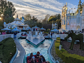 Scenic view of Disneyland's "It's a Small World" ride featuring colorful architecture, guests enjoying the boat ride, and lush greenery in the foreground.