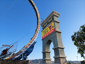Amusement park entrance sign featuring a colorful roller coaster track, promoting family-friendly attractions in a scenic outdoor setting.