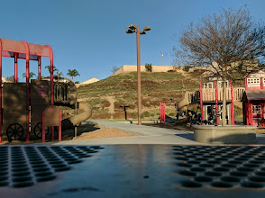 Playground equipment with slides and climbing structures in a scenic park setting, surrounded by green hills and clear blue sky, emphasizing family-friendly outdoor spaces in Corona.